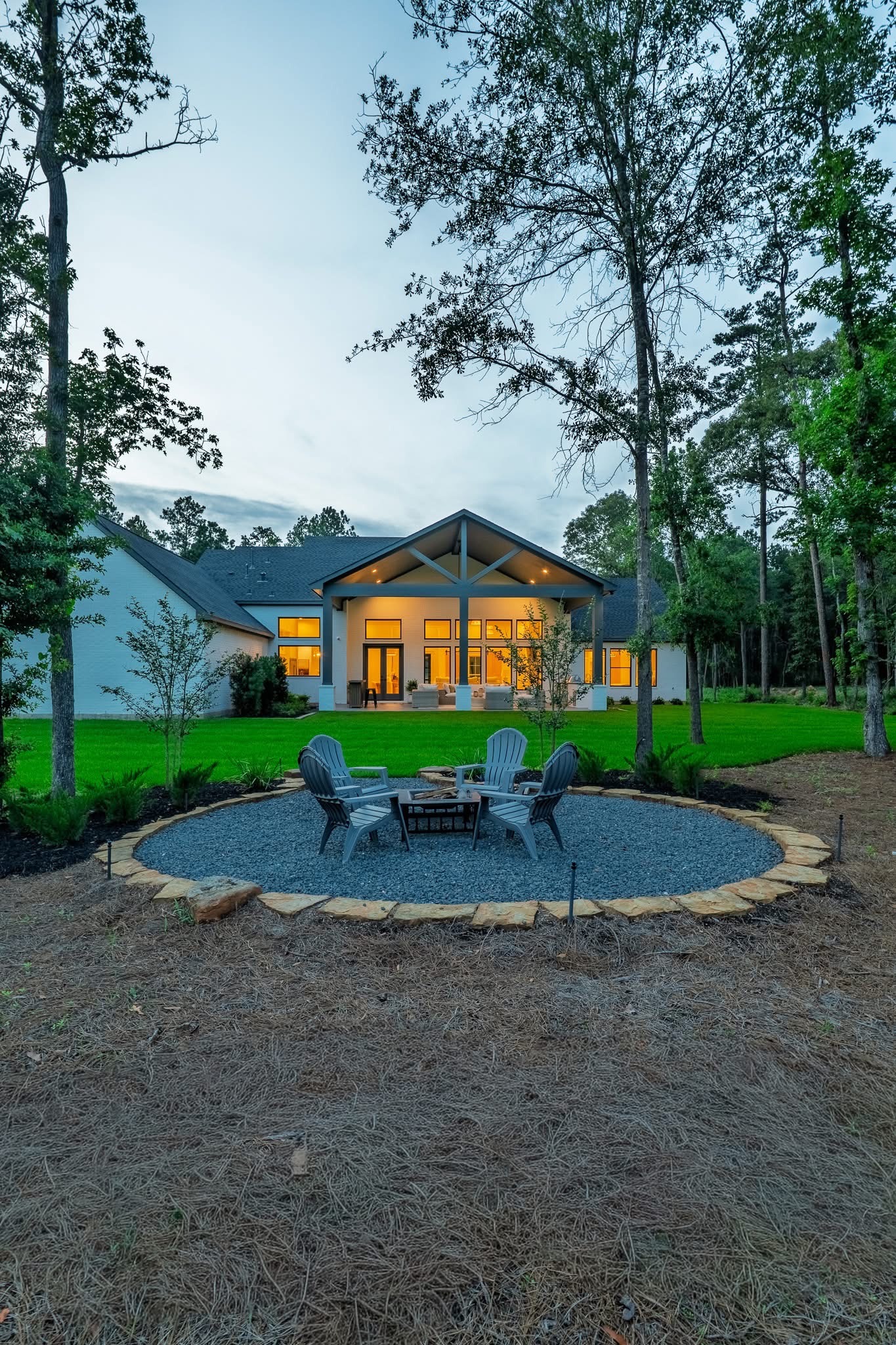 Custom home with a covered back porch and outdoor seating area among tall trees