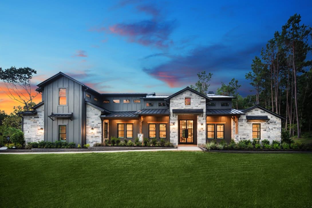 Custom home with stone exterior, metal roof and illuminated front porch at sunset