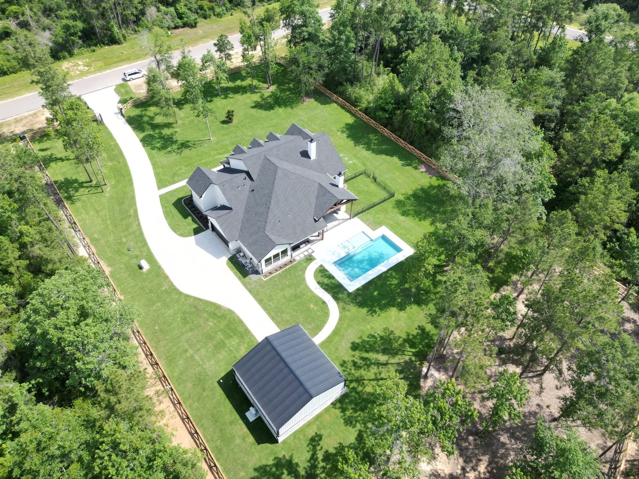 Aerial view of a home, swimming pool and detached shop with a spacious lawn surrounded by trees